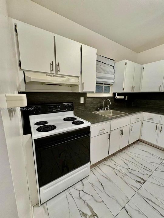 Kitchen featuring white shaker-style cabinetry with modern bar pulls, dark stone-finish backsplash, stainless steel sink with high-arc faucet, and large-format tile flooring with marble-pattern veining