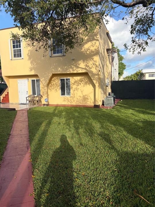 Two-story stucco exterior with a tiled entryway, concrete walkway, and fenced backyard featuring a grass lawn
