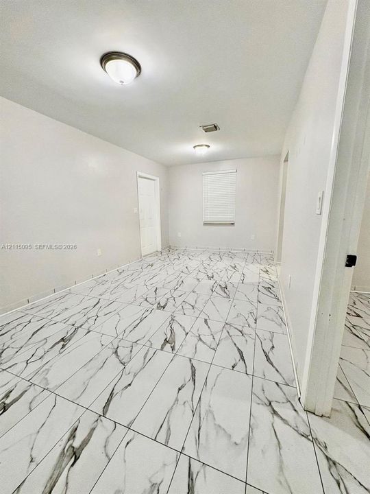 Rectangular tile flooring featuring a high-contrast marbled pattern, neutral wall palette, dual flush-mount ceiling light fixtures, and a single-panel interior door