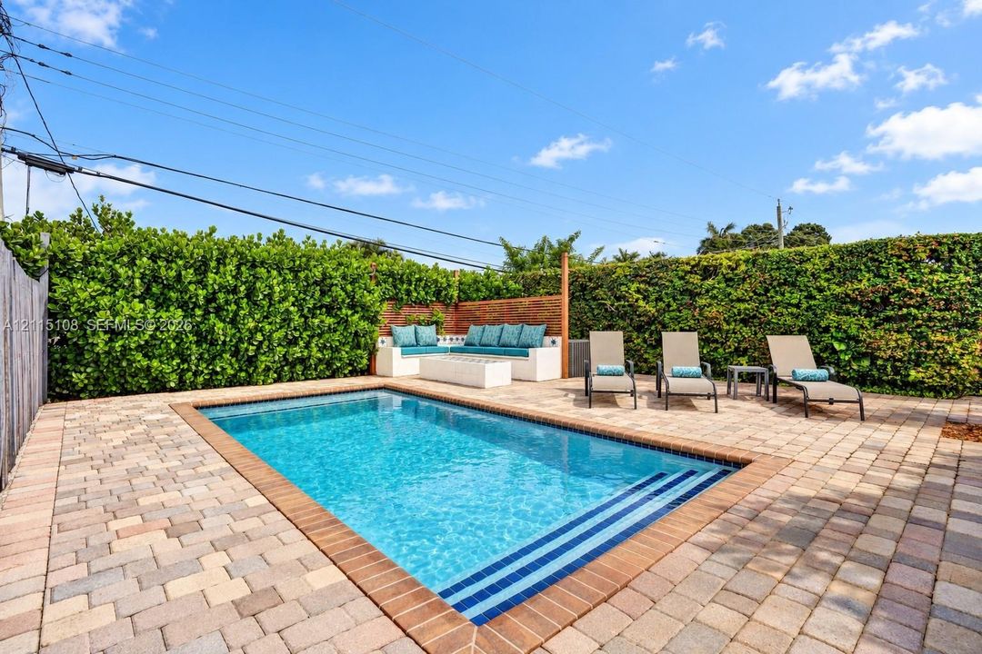 Outdoor swimming pool with integrated stairs and a brick paver deck enclosed by tall, manicured privacy hedges