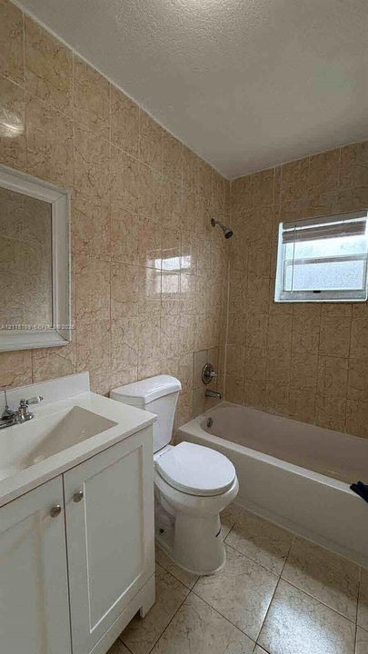 Bathroom featuring textured wall tiling, a white vanity with a rectangular sink, a tub-shower combination, and tiled flooring