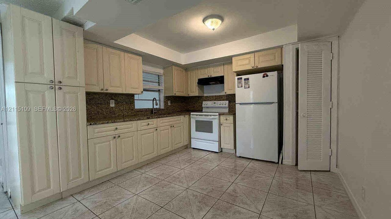 Kitchen featuring light-toned shaker cabinetry, stone countertops, tiled flooring, built-in floor-to-ceiling pantry storage, and a louvered-door closet