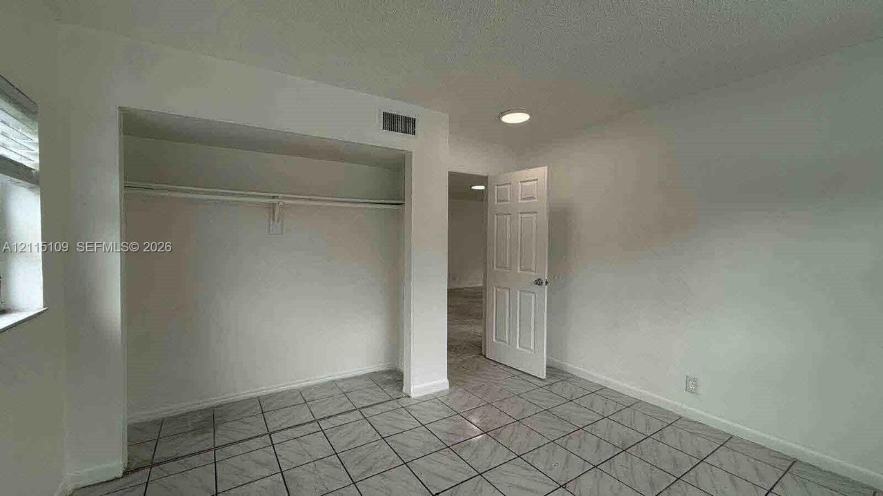 Room featuring tile flooring, built-in closet with overhead shelf, six-panel interior door, and flush-mount ceiling lighting
