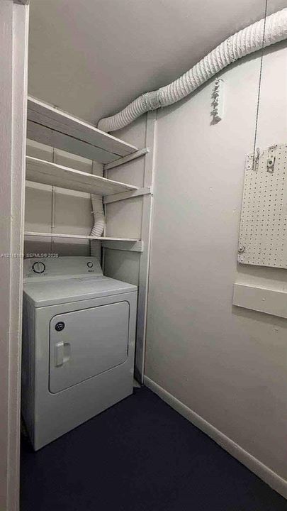 Laundry area featuring built-in wooden shelving, a mounted pegboard, and dark flooring
