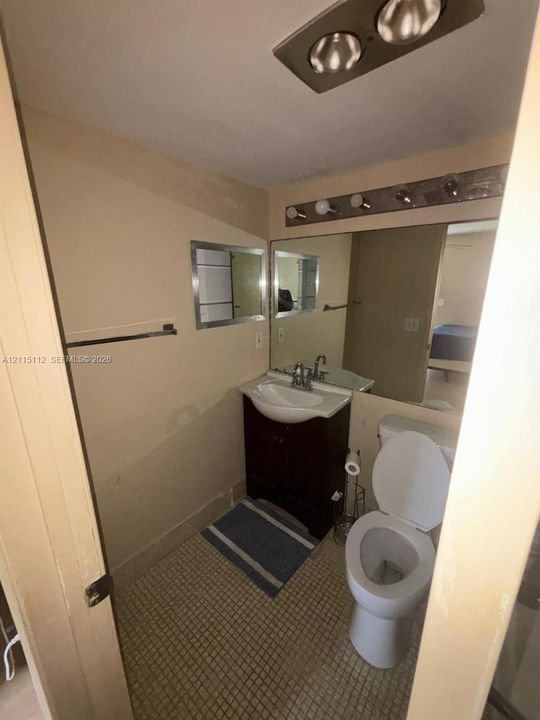 Bathroom featuring a vanity cabinet with a curved basin, wall-mounted mirror, multi-bulb vanity light, and tiled flooring