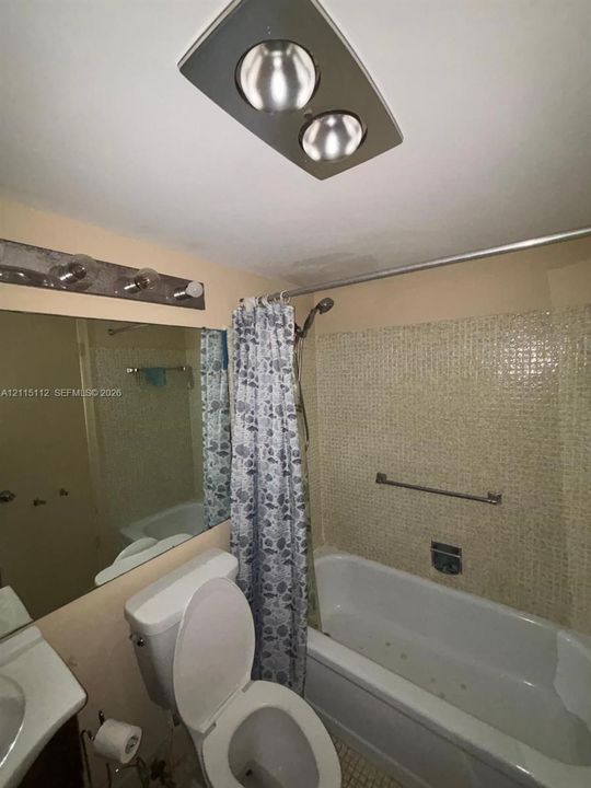 Bathroom featuring a shower-tub combination with mosaic tile surround, ceiling-mounted heating unit, and wall-mounted vanity mirror with multi-bulb light fixture