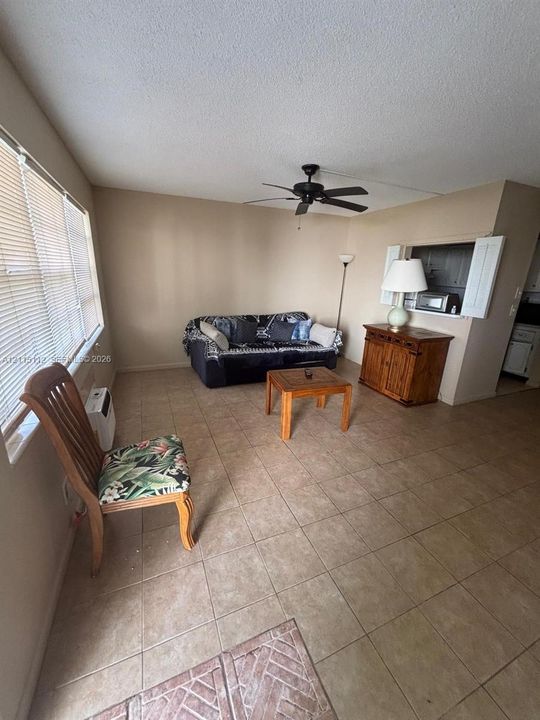 Neutral tile flooring, ceiling fan with integrated lighting, horizontal window blinds, and a built-in pass-through window with shutter doors