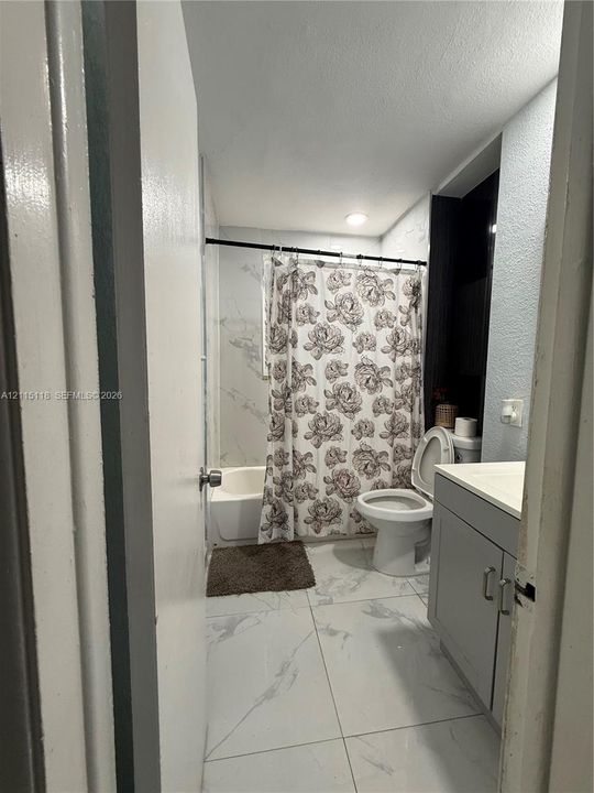 Bathroom featuring large-format tile flooring with a marble-finish, a grey vanity cabinet, and a shower-tub combination with tile surround