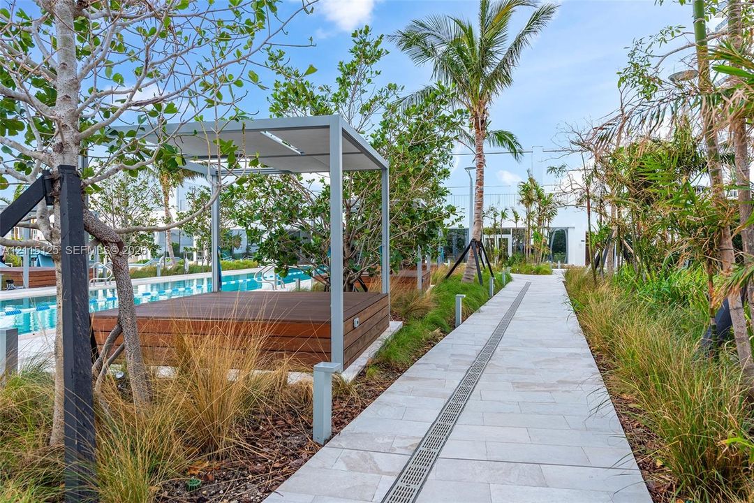 Swimming pool and spa area featuring natural stone deck surfacing, integrated metal handrails, and surrounding palm tree landscaping