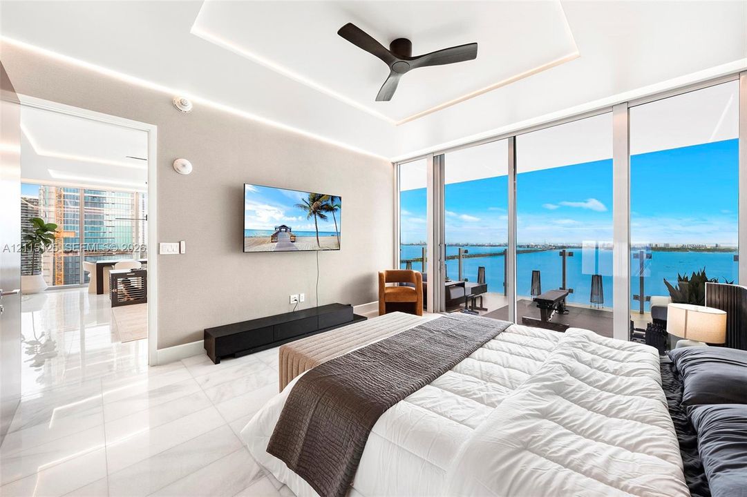 Floor-to-ceiling sliding glass doors, white tile flooring, tray ceiling with integrated recessed lighting, and a modern three-blade ceiling fan
