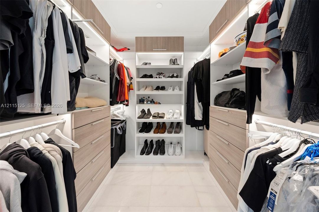 Walk-in closet featuring custom wood-finish cabinetry, built-in shelving with integrated lighting, and a multi-drawer dresser unit, paired with a bathroom showcasing a floating vanity, stone-surface countertop, and backlit oval mirror