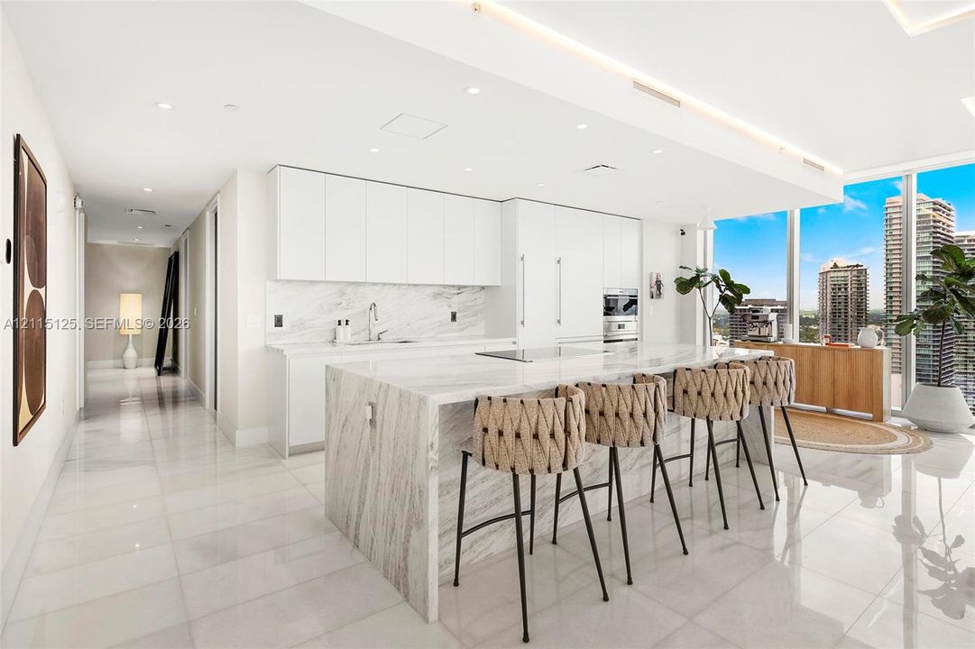 Floor-to-ceiling windows, blue accent wall, neutral tile flooring, and a private balcony