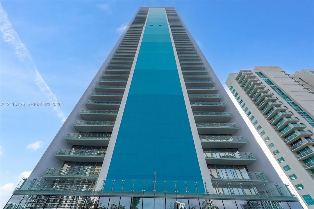 Expansive covered balcony featuring glass panel railings, floor-to-ceiling windows, and panoramic water scenery