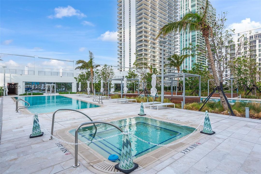 Expansive covered balcony featuring floor-to-ceiling glass doors, a glass panel railing, and water frontage