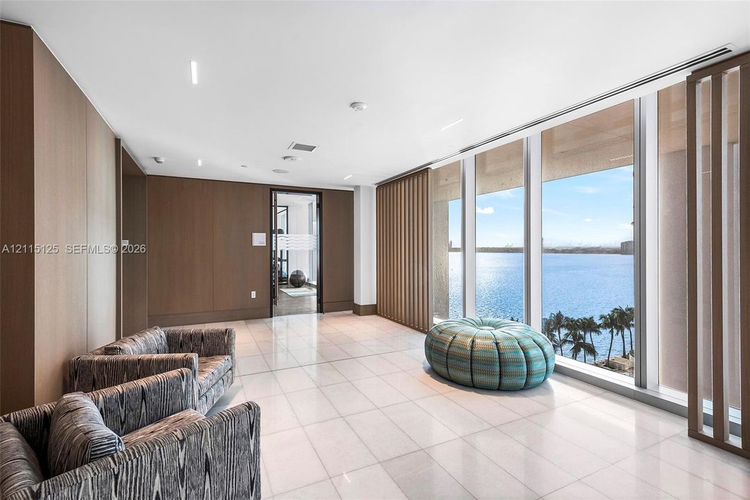Open-concept living space featuring floor-to-ceiling windows, recessed tray lighting, stone-finish flooring, a modern three-blade ceiling fan, and a kitchen equipped with integrated cabinetry and a stone-pattern backsplash