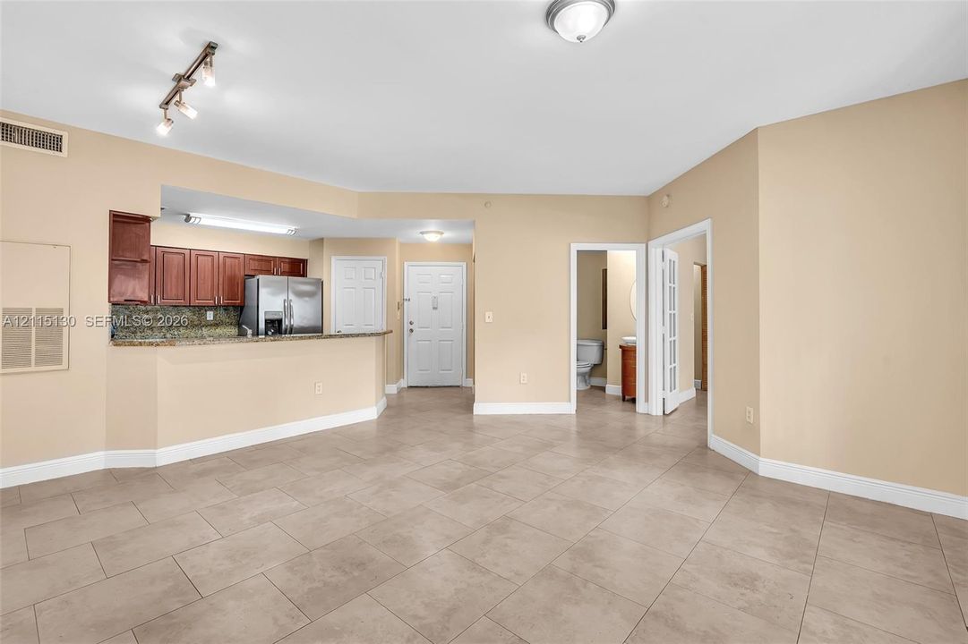Open-concept interior featuring large-format tile flooring, kitchen with granite countertops and wood cabinetry, stainless steel refrigerator, and recessed track lighting