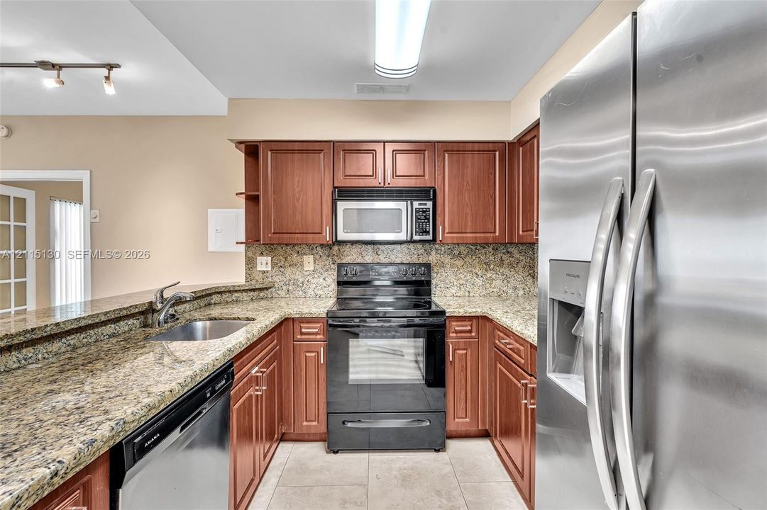 Kitchen featuring warm-tone cabinetry, stone-finish countertops, stainless steel appliances, and a double-basin undermount sink with a gooseneck faucet