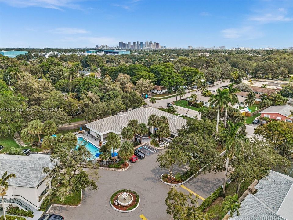 Aerial perspective featuring a central fountain, swimming pool with deck area, mature landscaping, and an urban skyline backdrop
