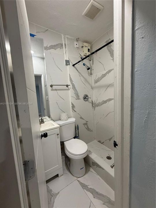 Bathroom featuring large-format, veined tile flooring and matching wall surround, white vanity cabinet with a integrated sink, and a chrome shower fixture