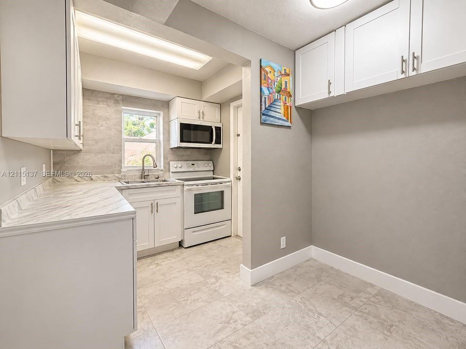 Kitchen featuring white cabinetry, solid-surface countertops, tile backsplash, built-in microwave, and large-format tile flooring