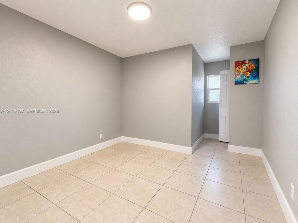 Neutral-toned wall finish, large-format neutral floor tiling, flush-mount ceiling lighting, and a multi-panel interior door