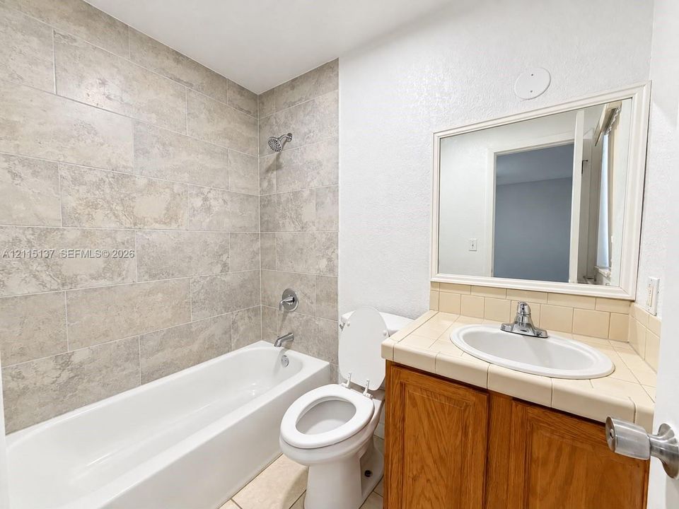 Bathroom featuring a tub-shower combination with large-format wall tile, wood-finish vanity cabinet with tile countertop, undermount sink, and framed wall-mounted mirror