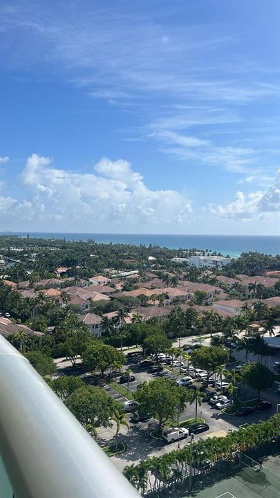 Elevated perspective featuring coastal horizon, mature tree canopy, and dedicated tennis court