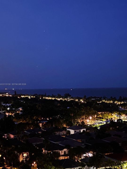 Elevated perspective of the coastal landscape featuring expansive water horizon and illuminated residential area