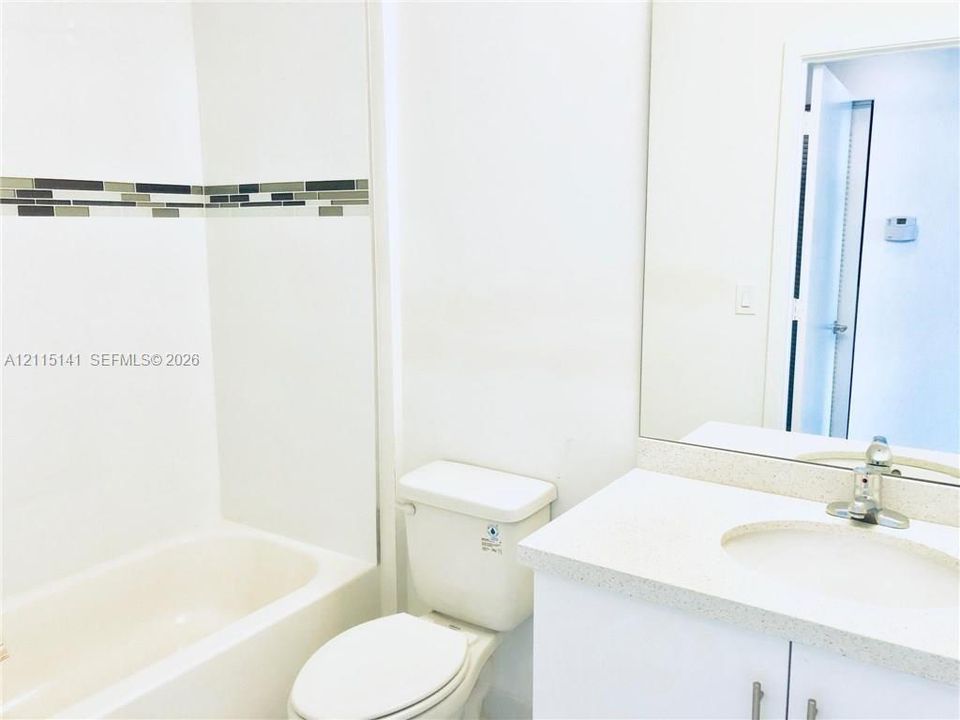 Bathroom featuring a vanity with a light-toned solid surface countertop, an undermount sink, a full-width wall mirror, and a bathtub with a decorative glass tile inlay