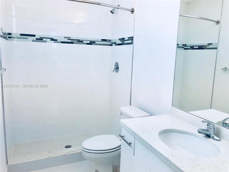 Bathroom featuring a white vanity with a light-toned solid surface countertop, an oval undermount sink, a walk-in shower with decorative mosaic tile inlay, and a wall-mounted mirror