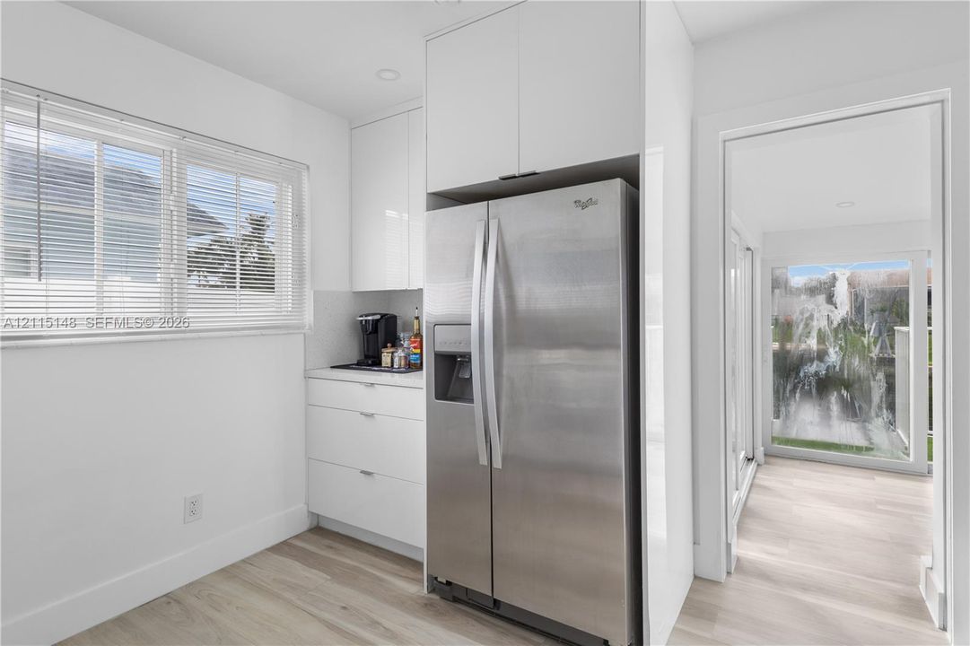 Glossy white flat-panel cabinetry, stainless steel refrigerator, horizontal window blinds, recessed ceiling lighting, and wood-finish flooring