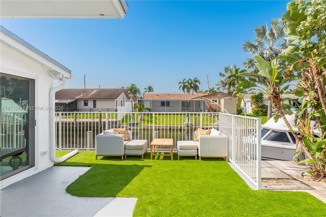 Waterfront patio featuring artificial turf, a white metal perimeter fence, and a wooden bulkhead