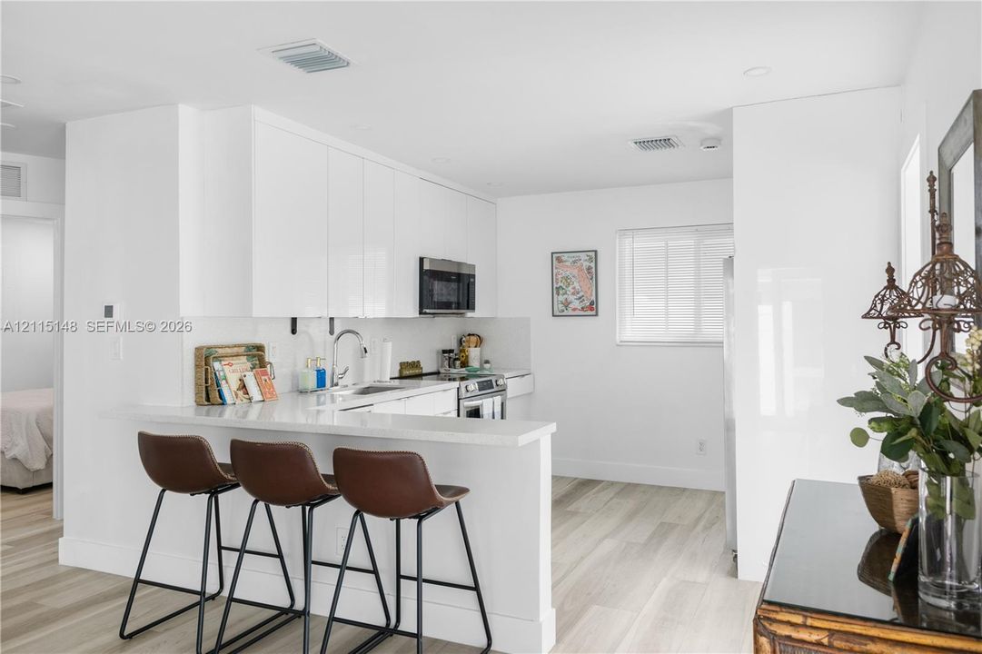 Kitchen featuring white high-gloss flat-panel cabinetry, a peninsula with a stone-surface countertop, stainless steel appliances, and wood-finish flooring