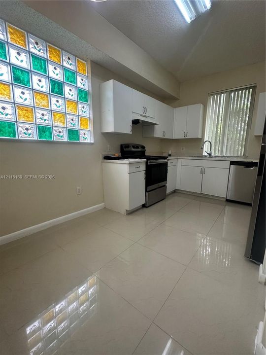 Kitchen featuring white cabinetry, large-format tile flooring, stainless steel appliances, and a glass block window with multicolor accents