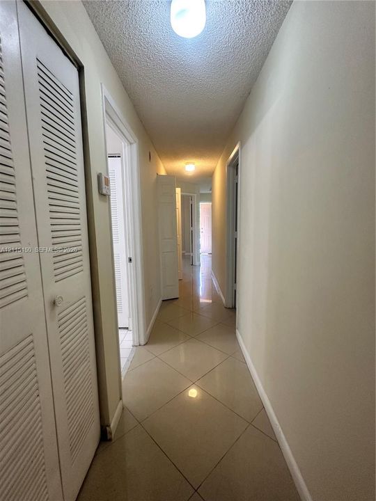 Hallway featuring neutral large-format tile flooring and louvered-style closet doors