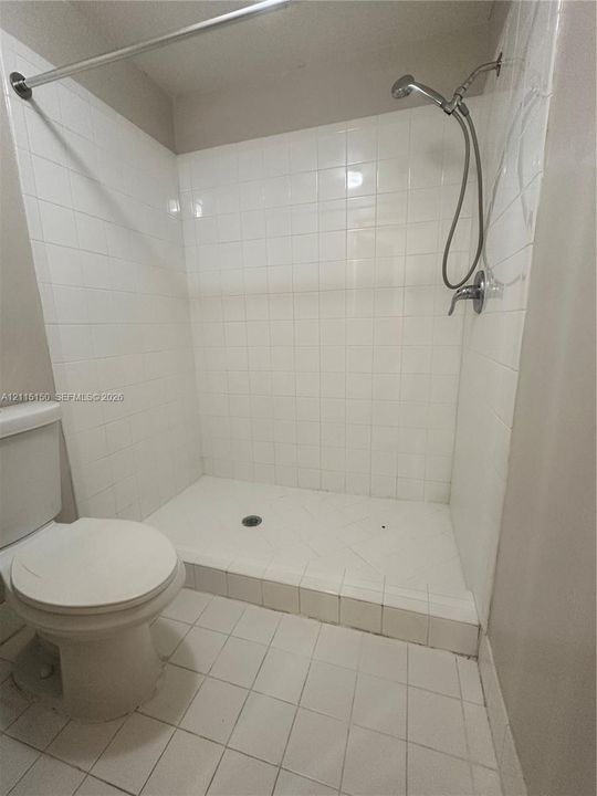Walk-in shower enclosure featuring white wall tiling, a raised tiled threshold, and a chrome handheld shower fixture, accompanied by a white porcelain toilet