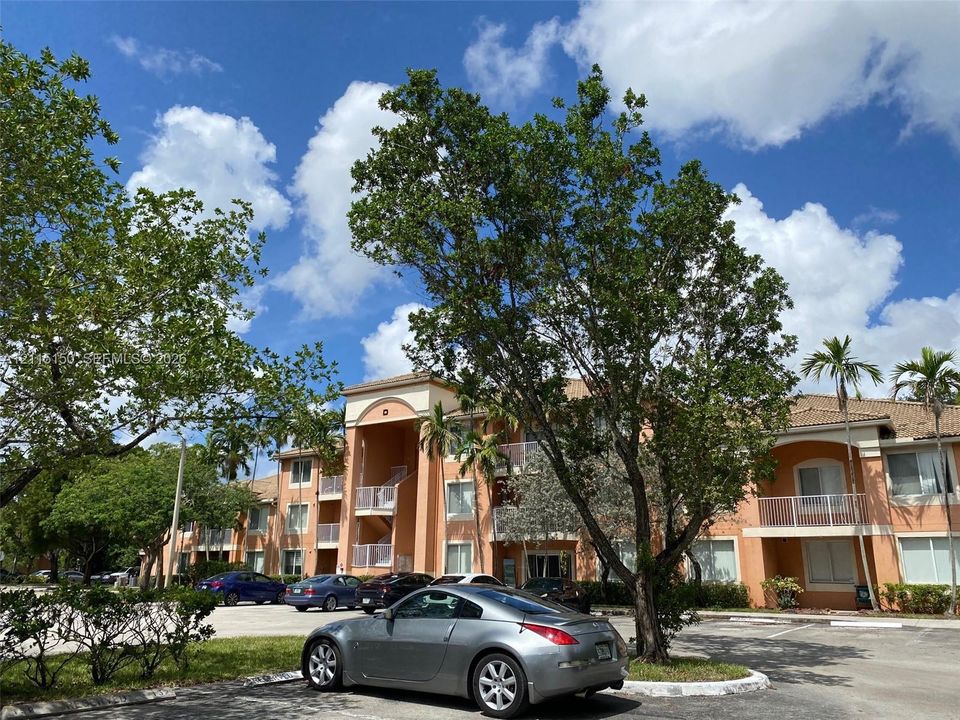 Multi-story building exterior featuring stucco siding, arched entryways, and private balconies with white railings