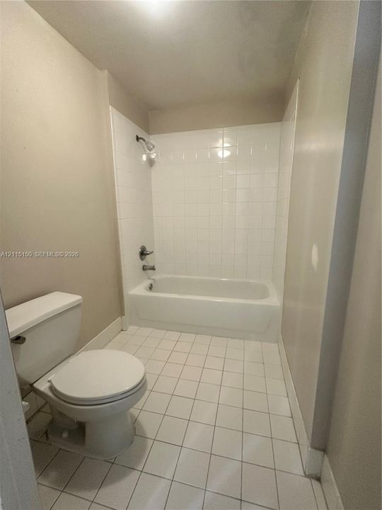 Bathroom featuring a white ceramic tile floor, bathtub with a white tile surround, wall-mounted shower head, and dual-handle plumbing fixture