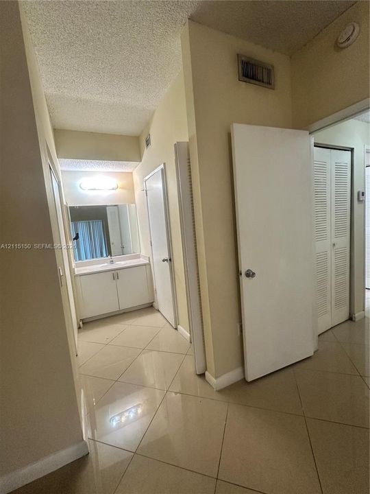 Large-format tile flooring, built-in vanity with integrated basin, expansive wall mirror, and louvered closet doors