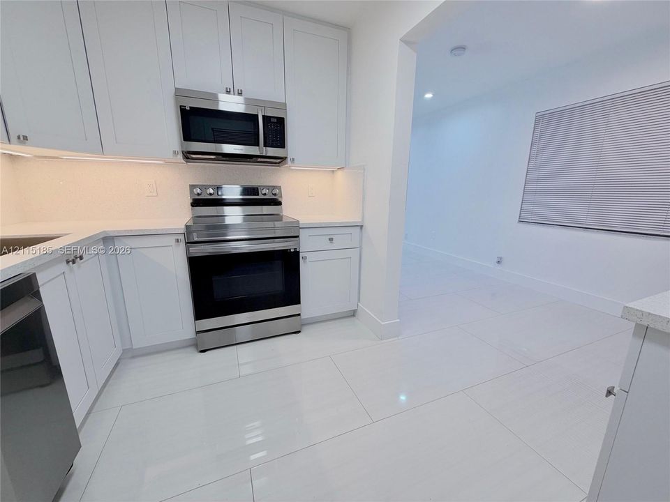 Kitchen featuring white shaker-style cabinetry, stainless steel appliances, under-cabinet lighting, solid surface countertops, and large-format porcelain tile flooring