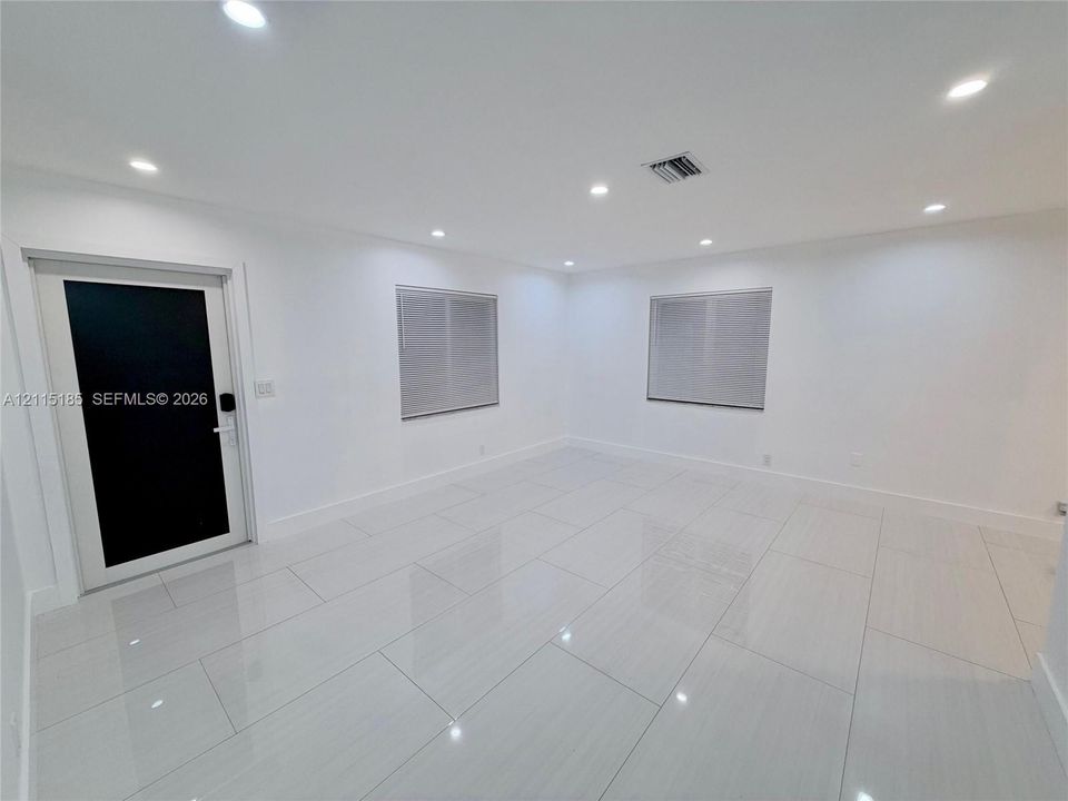 Interior space featuring high-gloss tile flooring, recessed ceiling lighting, and a modern black-paneled entry door with hardware