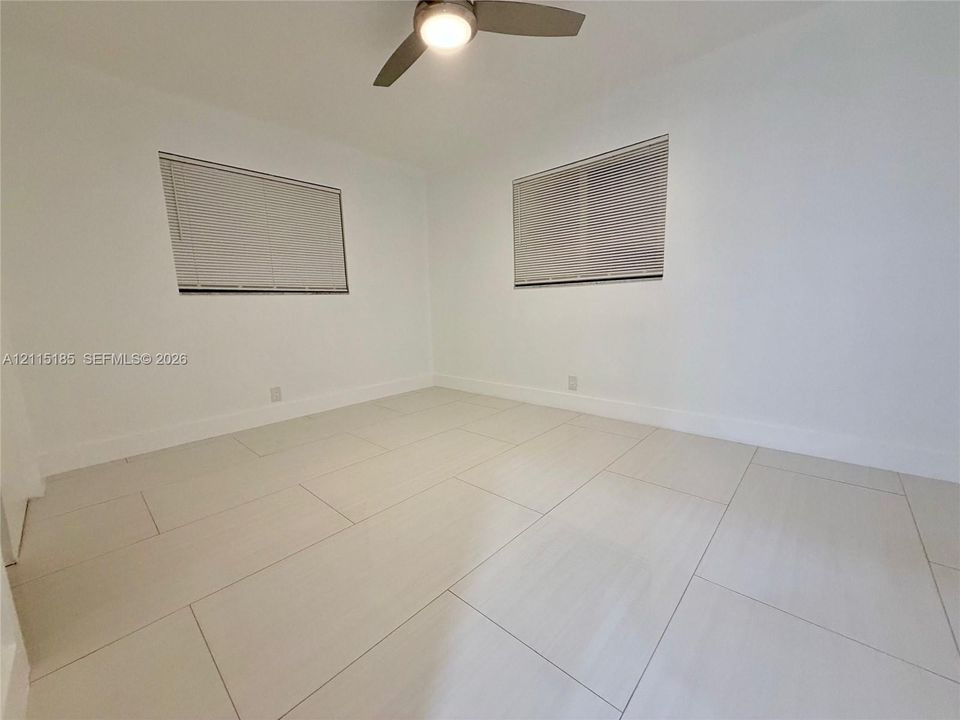 Bright interior featuring large-format tile flooring, neutral walls, two windows with horizontal blinds, and a central ceiling fan with integrated lighting