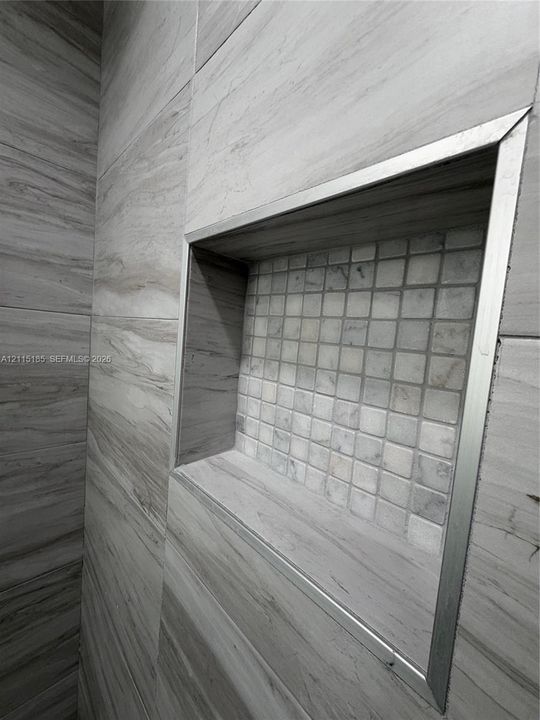 Recessed shower niche featuring large-format horizontal tile, square mosaic tile inlay, and brushed metal trim