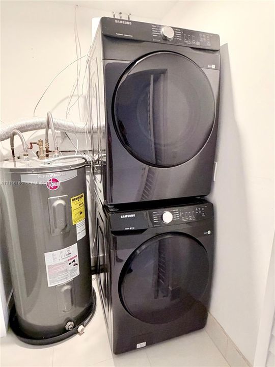 Stacked dark-finish front-load laundry appliances and a cylindrical water heater