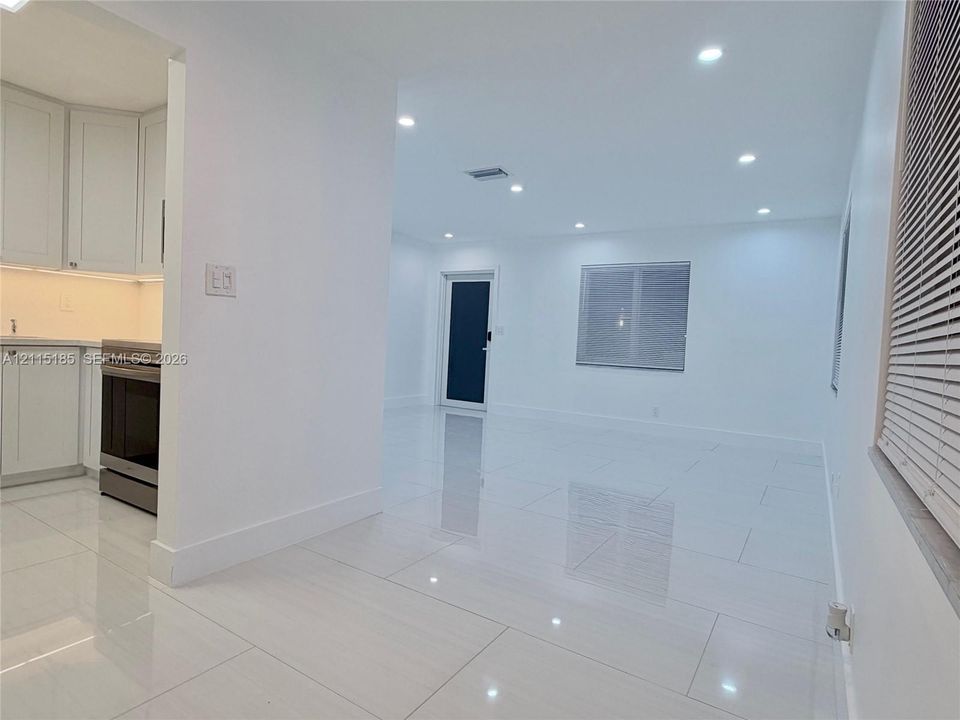 Open interior featuring large-format ceramic tile flooring, recessed ceiling lighting, white shaker-style cabinetry, and a dark-toned door