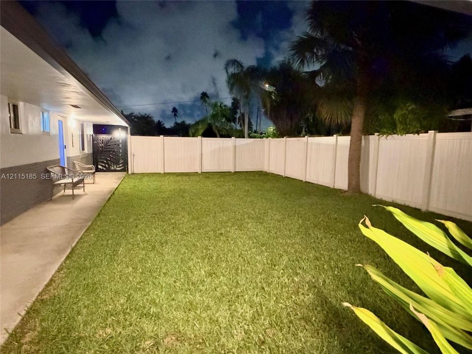 Private backyard featuring a concrete patio, white vinyl fencing, manicured lawn, and mature palm trees