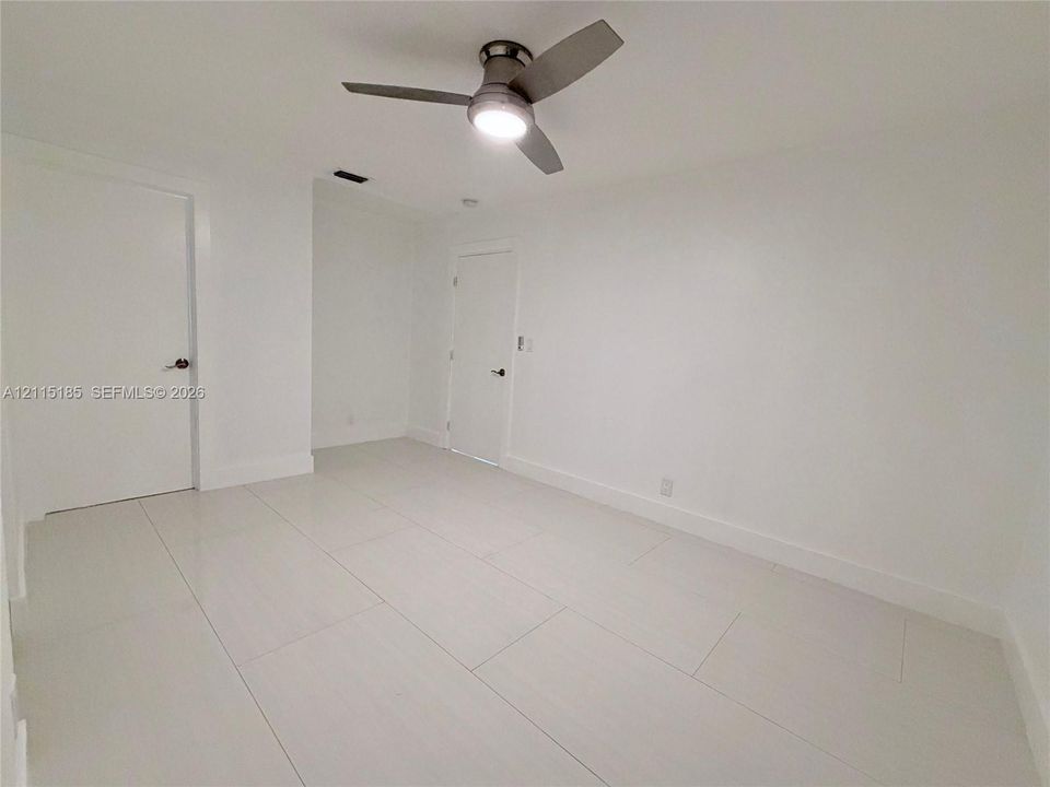 Interior space featuring large-format porcelain tile flooring, smooth wall finishes, two interior doors with matte-finish hardware, and a modern three-blade ceiling fan with integrated lighting