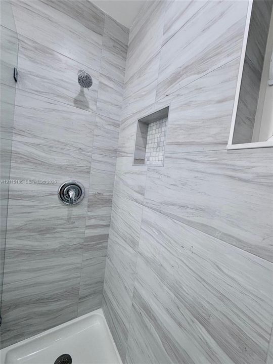 Shower enclosure featuring large-format neutral-toned tile, built-in recessed niche with mosaic accent, glass panel, and polished chrome shower fixtures