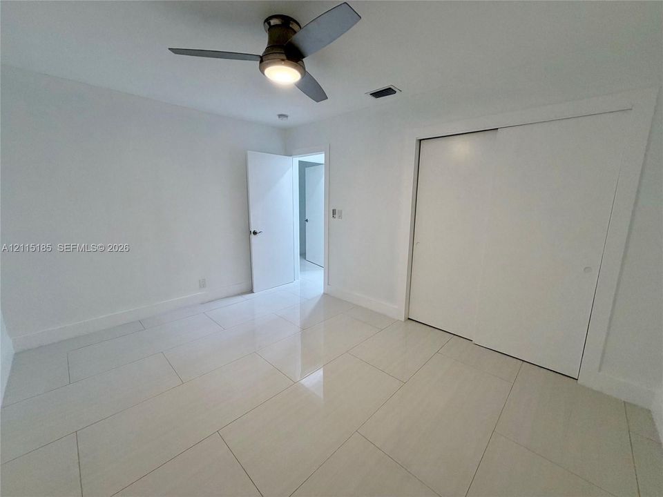 Neutral-toned interior space featuring polished large-format tile flooring, a dual-panel sliding closet, and a ceiling-mounted light fixture with an integrated fan