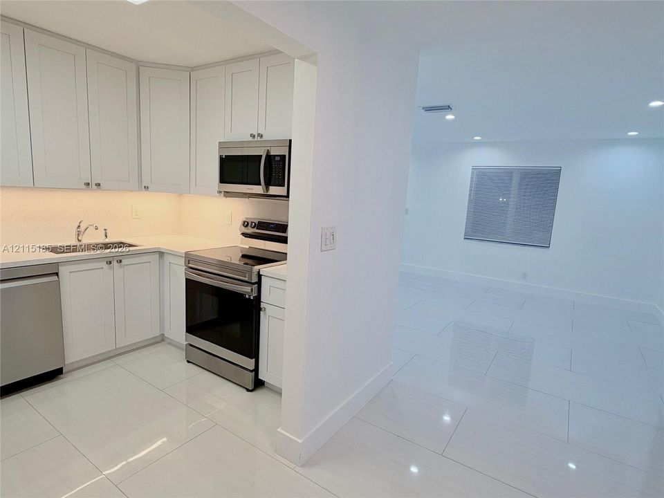 Kitchen featuring white shaker-style cabinetry, solid-surface countertops, and stainless steel appliances, complemented by large-format tile flooring and recessed lighting